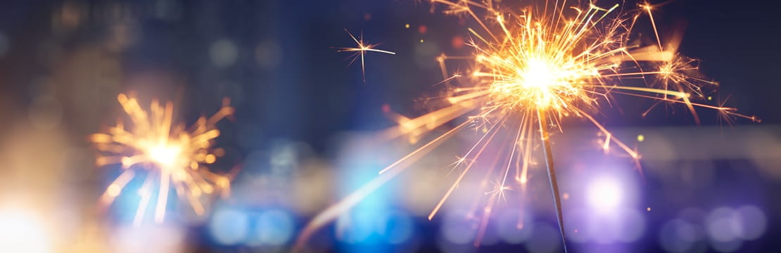 Close-up of sparklers glowing brightly against a blurred cityscape at night.